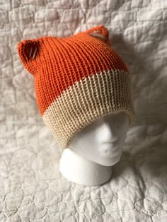 an orange and white knitted hat sitting on top of a mannequin head