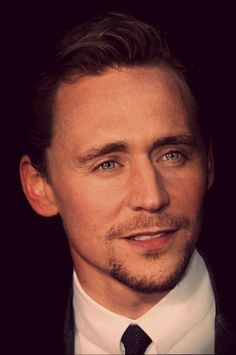 a close up of a person wearing a suit and tie with a black background, looking at the camera