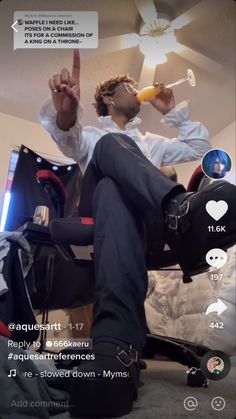 a man sitting on top of a bed next to a computer desk with a glass in his hand