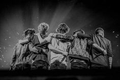 the backs of four people standing in front of a stage with their arms around each other