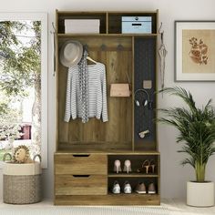 an open wooden cabinet with shoes and other items on the shelves next to a potted plant