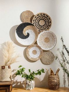 several woven baskets hanging on the wall above a wooden table with plants and vases