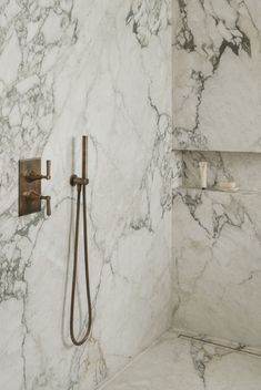 a bathroom with marble walls and flooring, shower head and hand held faucet