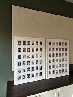 two white framed pictures sitting on top of a wooden shelf next to a wall mounted with photos