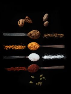 several different types of spices and spoons on a black background