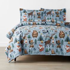 a bed covered in a blue comforter with animals and trees on it