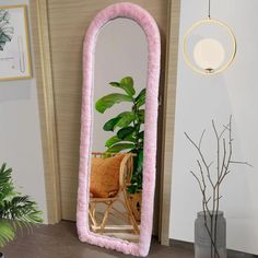 a large pink mirror sitting on top of a wooden floor next to a potted plant