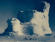 a group of people riding sleds down a snow covered slope next to an iceberg