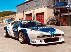 a white and blue bmw race car parked in front of a building with red doors