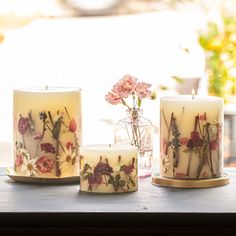 three candles sitting on top of a table with flowers in vases next to them