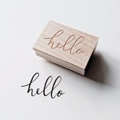 a rubber stamp with the word hello written in cursive writing on it, next to an ink pen