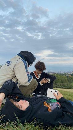 two people sitting in the grass looking at their cell phones while one person sits on the ground