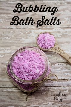 two jars filled with pink bath salts on top of a wooden table