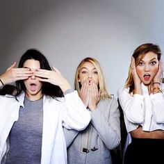 three women covering their eyes with hands while standing in front of a wall and looking surprised