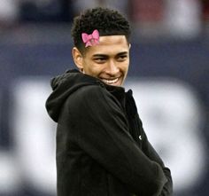 a man with a pink bow on his head smiles at the camera while wearing a black jacket