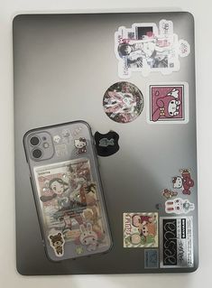 an open laptop with various stickers and magnets on the back cover, along with a cell phone