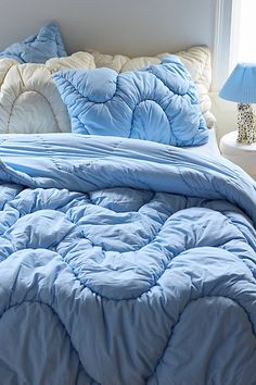 a bed with blue and white comforters in a bedroom next to a lamp on a table