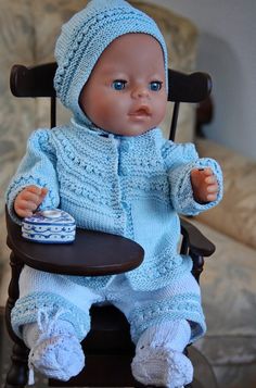 a baby doll sitting in a rocking chair with a blue knitted outfit and hat