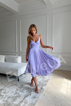 a woman in a purple dress standing on a white carpet with her hand out to the side