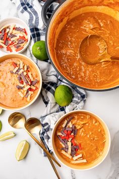 three bowls of soup on a table with limes and spoons next to them