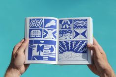 a person holding an open book with blue and white designs on it's pages