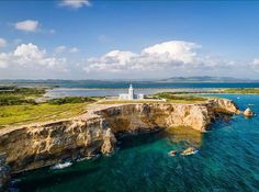 an aerial view of a lighthouse on top of a cliff next to the ocean with blue water