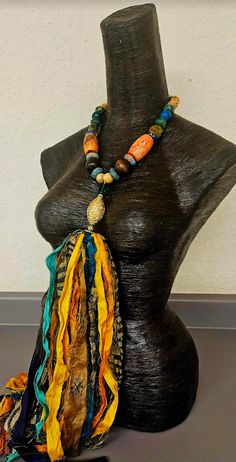 A single strand of mixed beads supports a distressed sari silk multiple strand ribbon pendant. The necklace includes orange magnesite barrels, wood beads, African recycled glass, Hubei turquoise, chrysocolla, jade, shiny gold tone rounds, an emerald green faceted crystal, a shiny gold tone repousse bicone bead, rhinestone rondelles and an etched brass round. The necklace does have some weight. Adjusts from 20-23" with gold tone hardware and a lobster claw clasp. The ribbon colors include orange, navy-turquoise-teal blue, gold, and a neutral animal print. I deliberately left the ribbons long so taller women could trim to their preferred length. From the Atelier of Kat Kouture. Rocker Chic Accessories, Hubei Turquoise, Sari Silk Ribbon, Ribbon Jewelry, Unique Pendant Necklace, Statement Bib Necklace, Chest Piece, Mermaid Necklace, Sari Silk