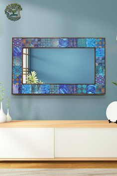 a blue mirror hanging on the wall above a white dresser with vases and potted plants