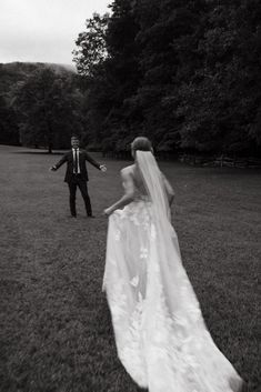 the bride and groom are walking through the grass in black and white, with trees in the background