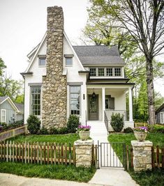 a white house with a stone chimney and fenced in lawn area next to it