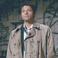 a man in a trench coat looking up at something with graffiti on the wall behind him