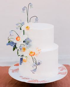 a three tiered white cake with flowers on the top and bottom, sitting on a wooden table