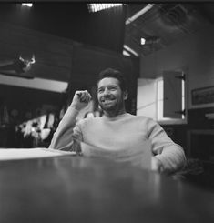 a black and white photo of a man sitting at a table with his arm in the air