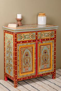 an ornately painted sideboard with candles on top and two vases in the corner