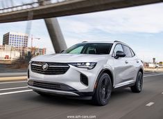 a white buick suv driving down the road in front of a bridge with buildings behind it