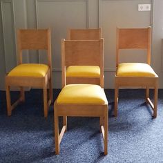 four wooden chairs sitting next to each other on a blue carpeted floor in front of a wall