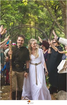 a man and woman dressed in medieval clothing are walking through the woods with their hands in the air