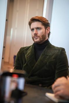 a man sitting at a table with a cup in front of him and looking off to the side