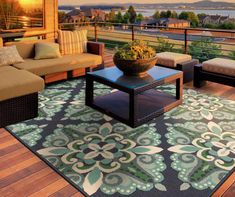 an outdoor living area with couches, tables and rugs on the wooden deck