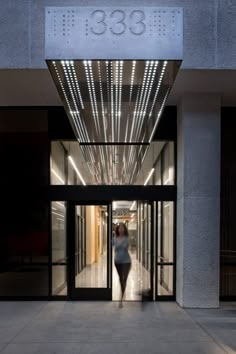 a woman is walking out of the entrance to an office building with lights on it