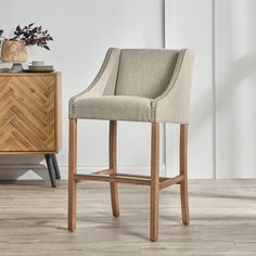 an upholstered bar stool next to a wooden dresser with a vase on it