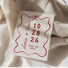 a red and white save the date sticker on top of a sheet of cloth