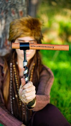 a woman with long hair is holding a wooden stick in front of her face while sitting on the grass