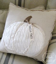 a white pumpkin pillow sitting on top of a couch next to a pillow with a ribbon