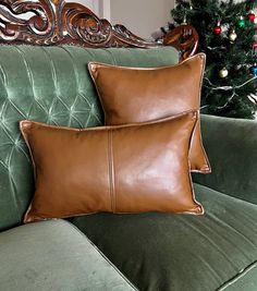 two brown leather pillows sitting on top of a green couch next to a christmas tree