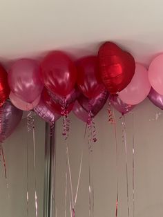 pink and red balloons are hanging from the ceiling in front of a mirror with streamers