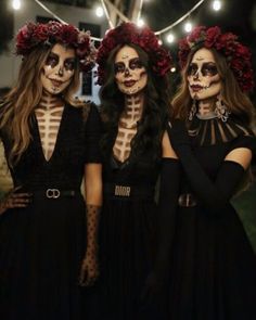 three women with skeleton makeup and flowers on their heads are standing in front of string lights