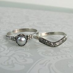 two silver rings sitting on top of a table next to each other and one has a pearl in the middle