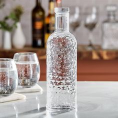 a glass bottle sitting on top of a counter next to wine glasses