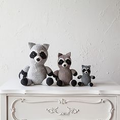 three stuffed raccoons sitting on top of a white dresser